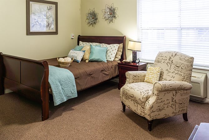 A cozy bedroom with a wooden bed, decorative pillows, and an armchair beside a lamp.