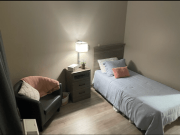 A cozy bedroom with a single bed, nightstand, and a lamp providing soft lighting.