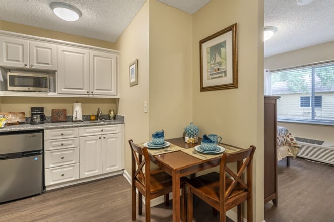 A cozy kitchen dining area with a small table set for two, featuring white cabinets and home decor.