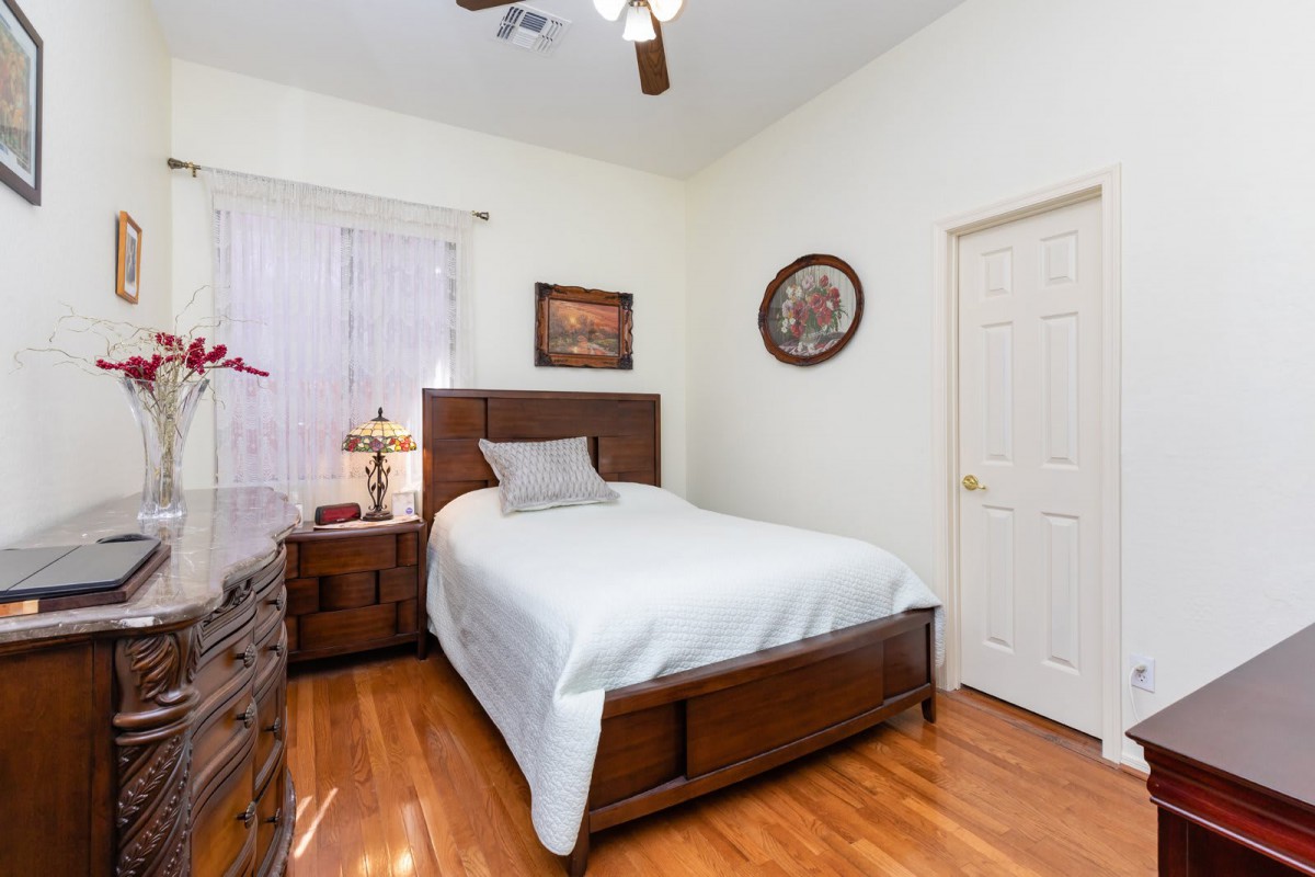 A cozy bedroom with a wooden bed and furniture, featuring a lamp and paintings on the wall.