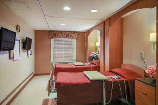 A cozy hospital patient room equipped with two beds and a warm color scheme.