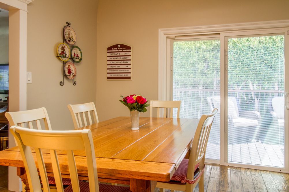 A cozy dining room with a wooden table and chairs, featuring a vase of flowers as the centerpiece.