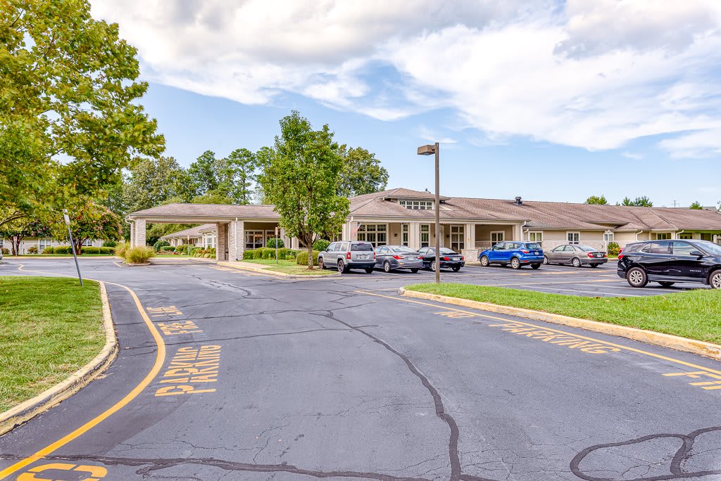 A view of a building with an adjacent parking lot, surrounded by trees and under a cloudy sky.