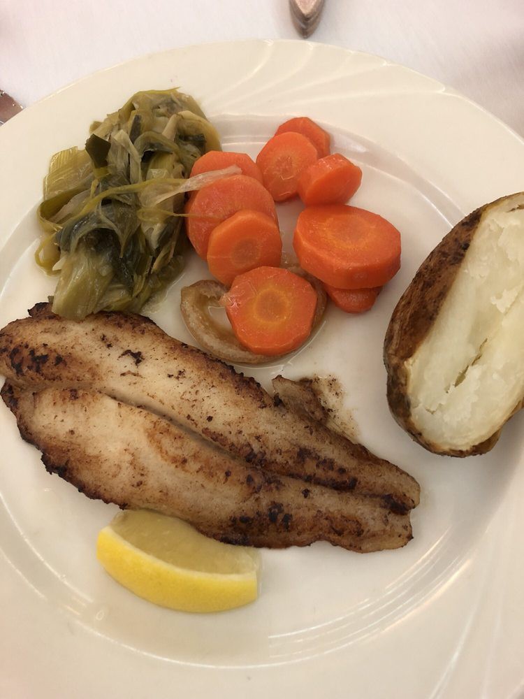 A plate of grilled fish served with carrots, cabbage, a baked potato, and a lemon wedge.