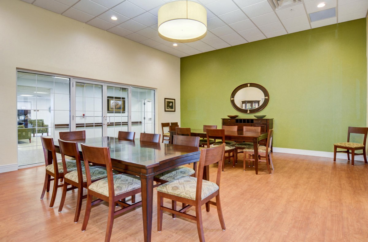 A well-furnished dining room with a large table, chairs, and a mirror on the green accent wall.