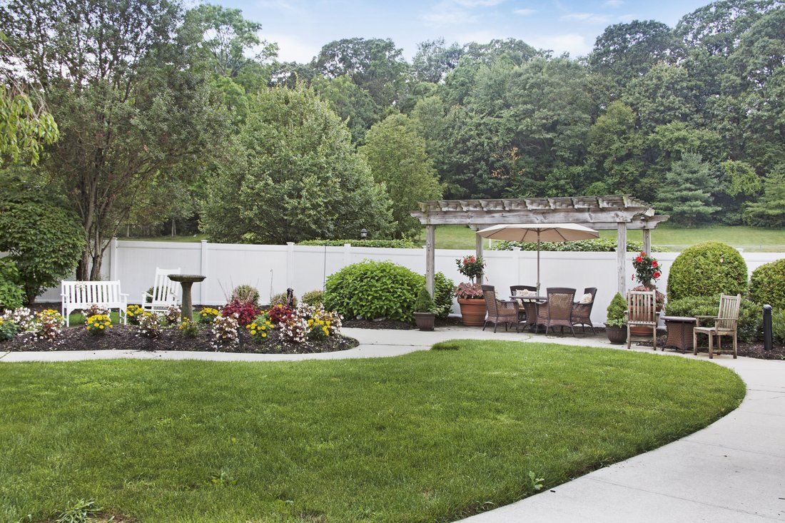A beautifully landscaped garden with a lawn, outdoor seating, and lush greenery against a backdrop of trees.