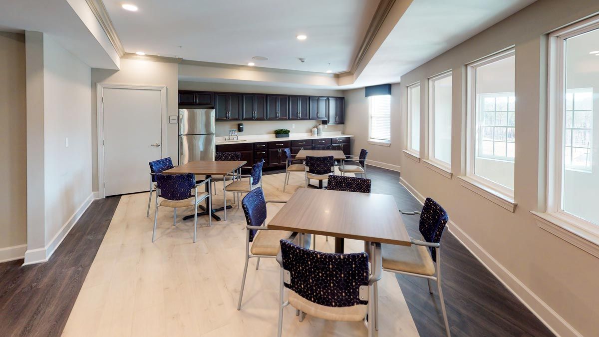 A modern kitchen and dining area with tables and chairs, featuring large windows.