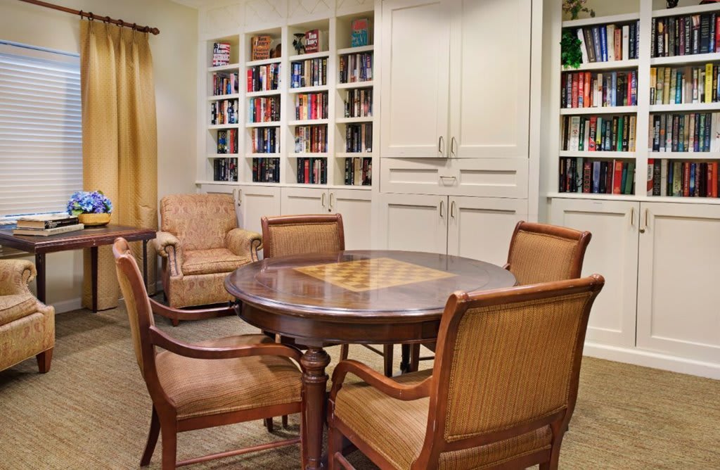 A cozy reading room with a round table surrounded by chairs, and bookshelves filled with books.