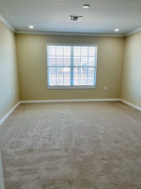 An empty room with beige walls, carpeted flooring, and a large window.