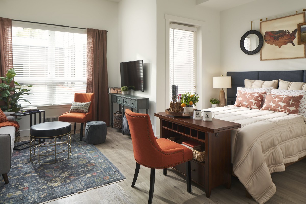 A cozy bedroom with modern furnishings, featuring a bed, chairs, a TV, and decorative elements.