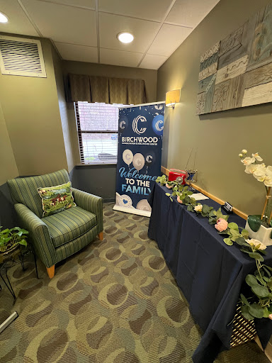 A cozy waiting area featuring a green chair, decorative table with flowers, and an informative banner.