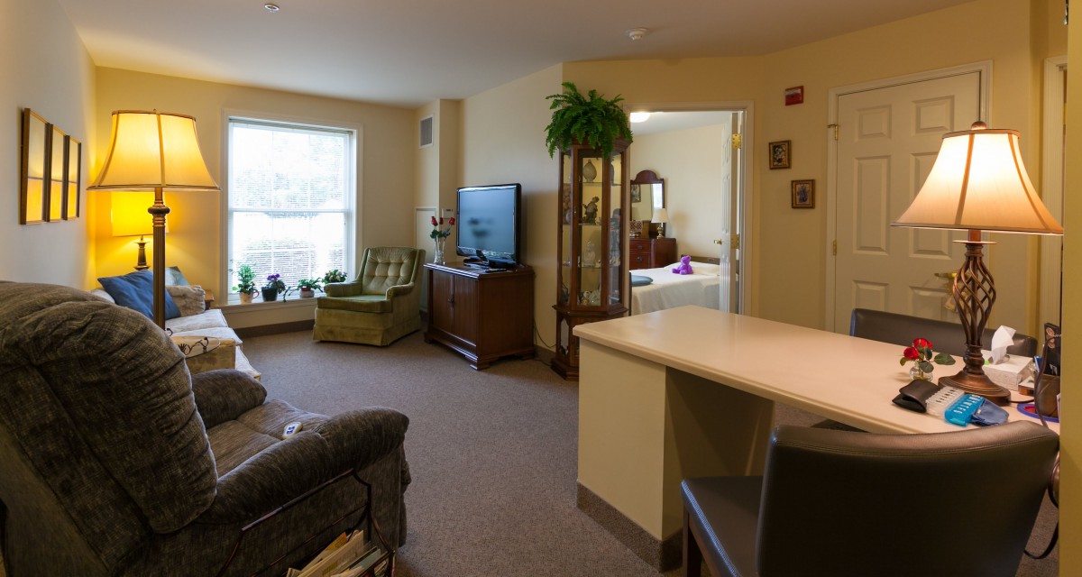 A cozy living space with a view into the adjacent bedroom, featuring comfortable furniture and decorative plants.
