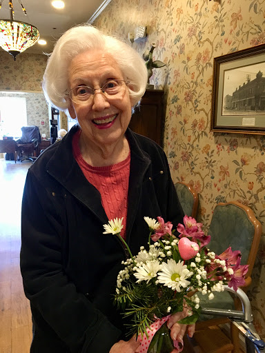 A joyful elderly woman holding a bouquet of flowers in a charming indoor setting.