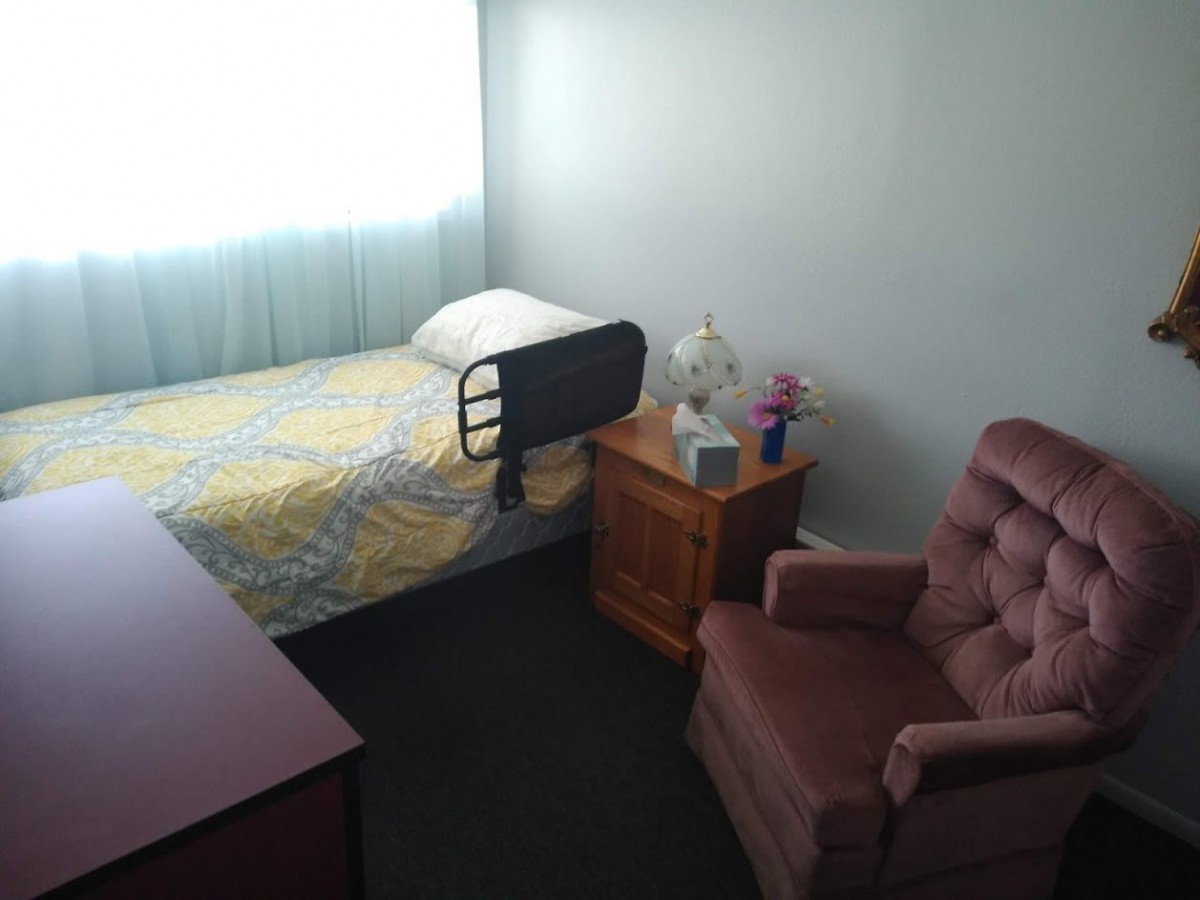 A small, minimalist bedroom with a single bed and an armchair.