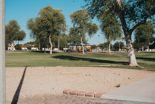 A serene park scene featuring a playground surrounded by lush greenery and clear blue skies.