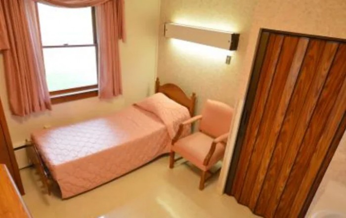 A simple bedroom with a single bed, pink bedding, and a chair by the window.