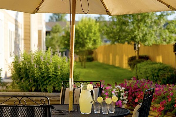 A sunny patio setting with a table featuring a pitcher of lemonade and glasses under an umbrella.