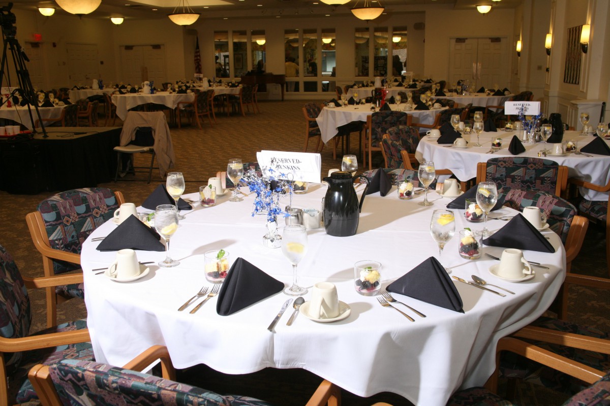 A formal banquet hall set up with elegantly arranged tables, featuring black napkins and white tablecloths.