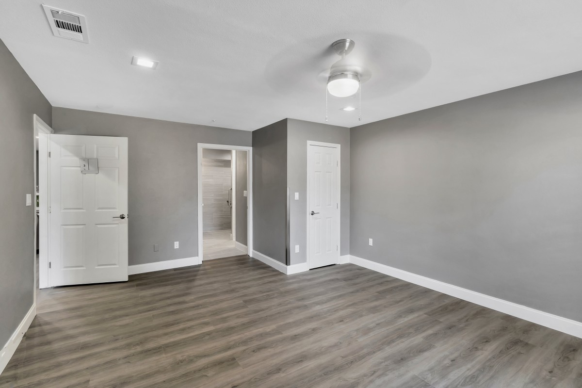 A modern empty room with gray walls and hardwood flooring, featuring a ceiling fan and recessed lighting.