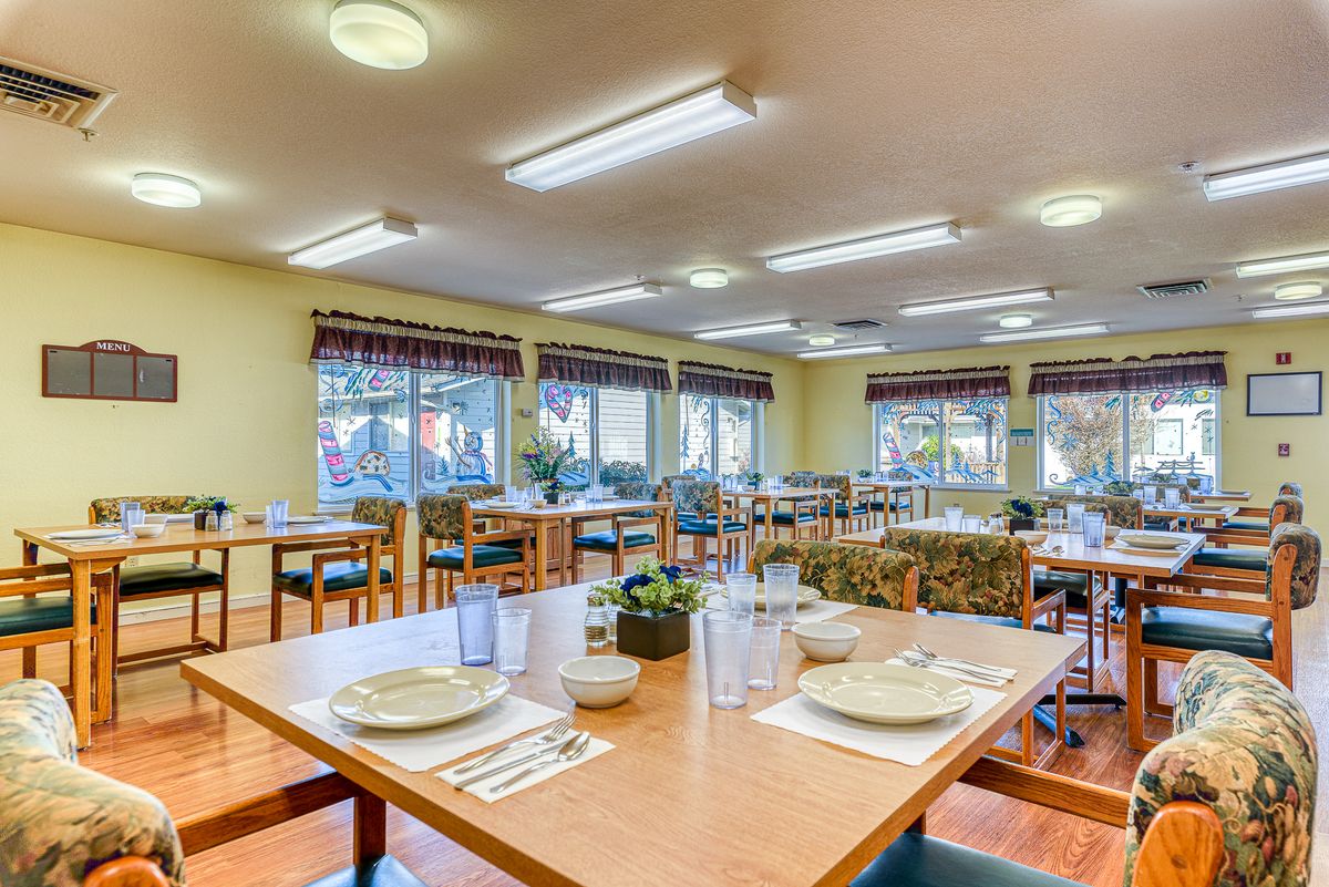 A spacious dining room with neatly arranged tables and chairs, illuminated by ceiling lights and natural daylight from large windows.