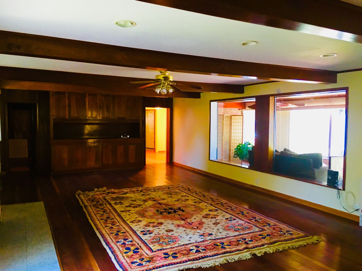 Spacious living room with wooden beams, large rug, and ceiling fan.