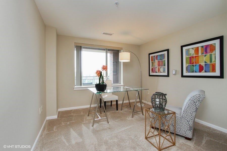 A modern home office setup featuring a glass desk, stylish chair, and decorative artwork.