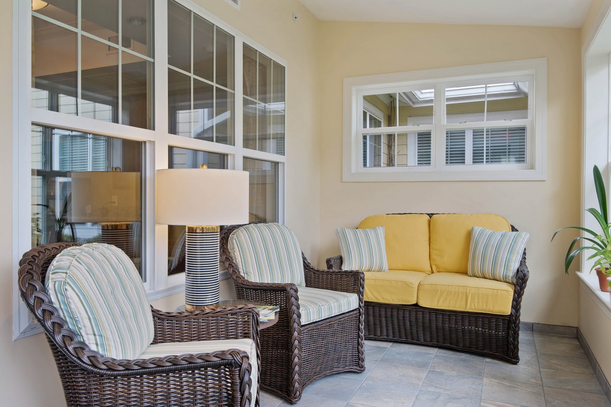 A cozy sunroom with wicker furniture and bright yellow cushions, complemented by a stylish lamp.