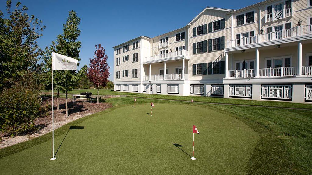 A scenic view of a putting green in front of a multi-story apartment building on a sunny day.