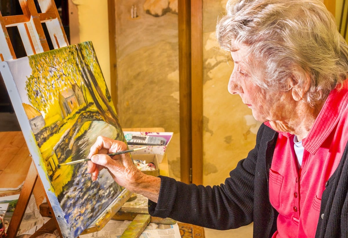 An artist focuses intently as she paints on a canvas indoors.