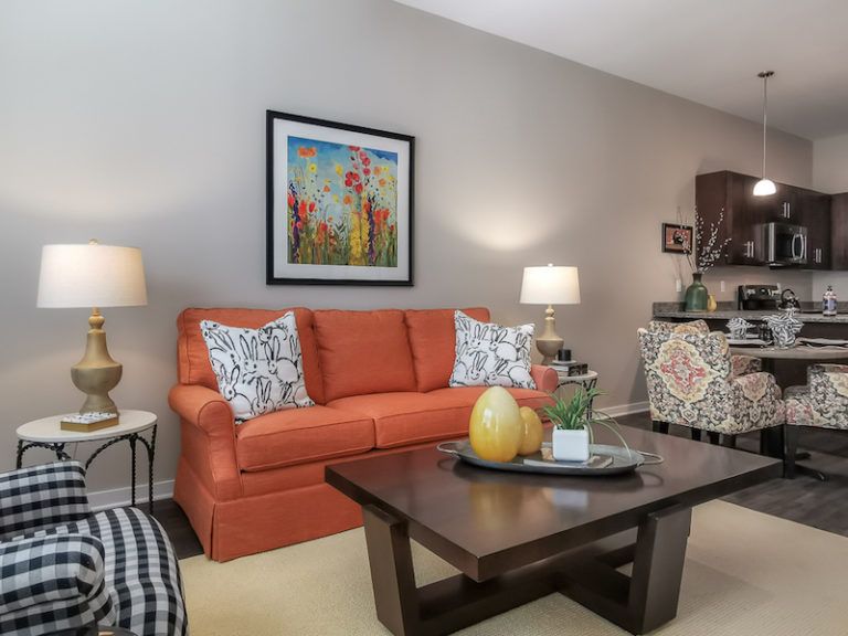 A cozy living room with an orange sofa, colorful artwork, and a wooden coffee table adorned with decorative items.