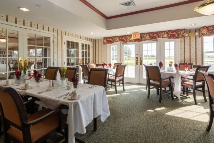 A well-lit dining room with neatly arranged tables and chairs, featuring large windows and elegant decor.