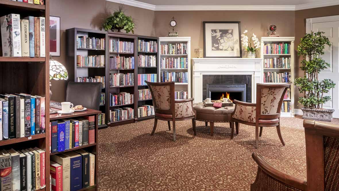 A cozy library with bookshelves, a fireplace, and comfortable armchairs.