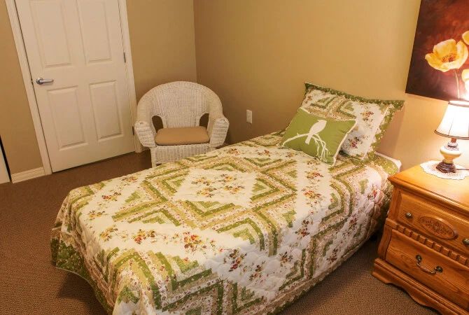 A cozy bedroom with a single bed adorned with a patterned quilt and a wicker chair in the corner.