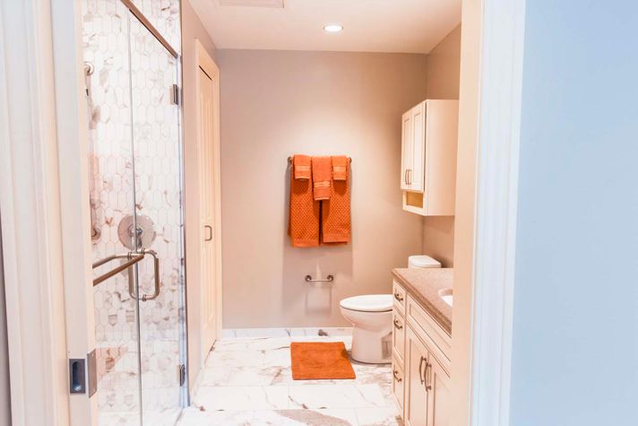 A modern bathroom with orange towels, featuring a shower, sink, and marble flooring.