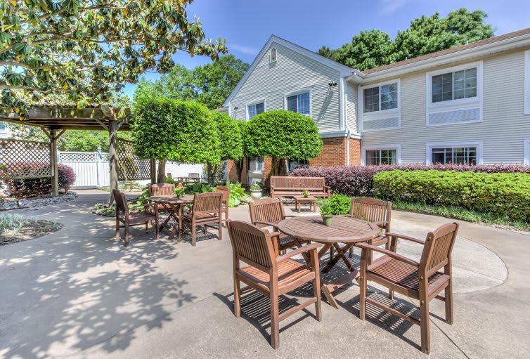 A sunny outdoor patio area with wooden tables and chairs surrounded by greenery.
