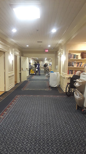 A well-lit hallway featuring bookshelves, a wheelchair, and cleaning equipment.