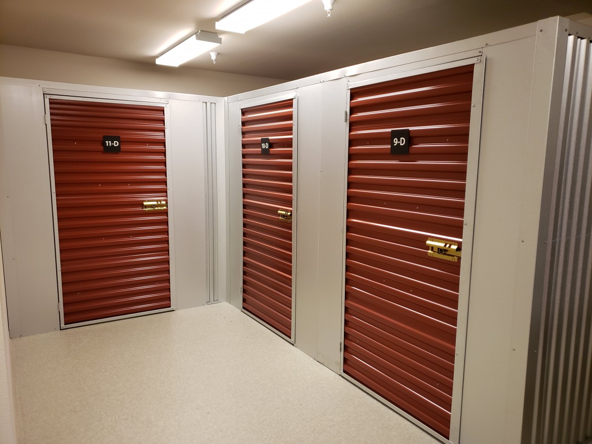 A well-lit corridor with multiple storage units featuring red shuttered doors.