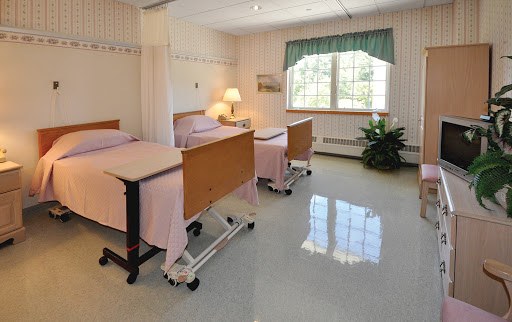 A clean and well-lit hospital patient room with two beds, equipped with lamps and a window providing natural light.