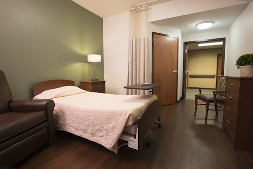 A hospital room with a bed, lamp, and chairs, creating a comfortable healthcare setting.