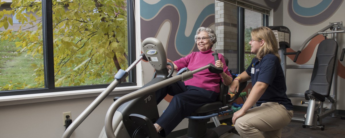 An elderly woman enjoying a workout on a recumbent bike indoors.