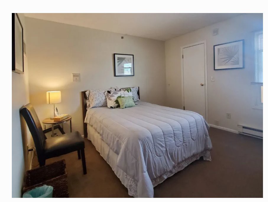 A cozy bedroom with a neatly made bed, a chair, and a lamp.