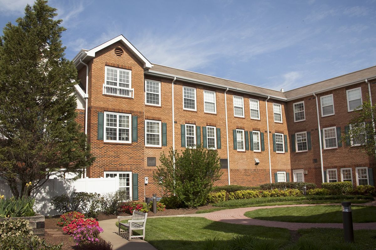 A brick residential building with a landscaped garden under a clear blue sky.