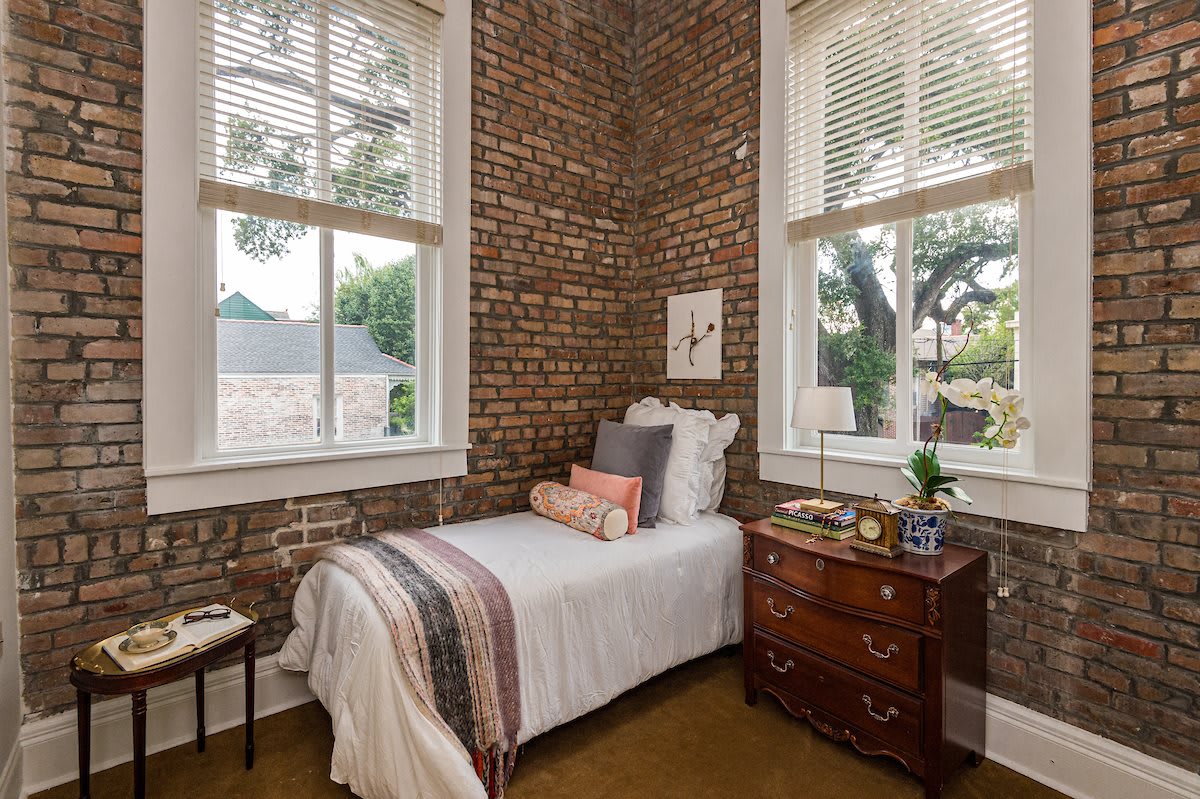 Cozy bedroom with exposed brick walls and large windows letting in natural light.