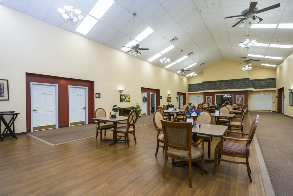 A spacious dining area with tables and chairs, featuring ceiling fans and a wooden floor.