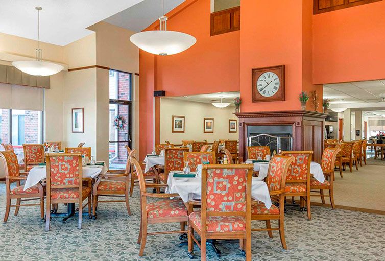 A neatly arranged dining area with patterned chairs and tables, warm lighting, and a prominent wall clock.