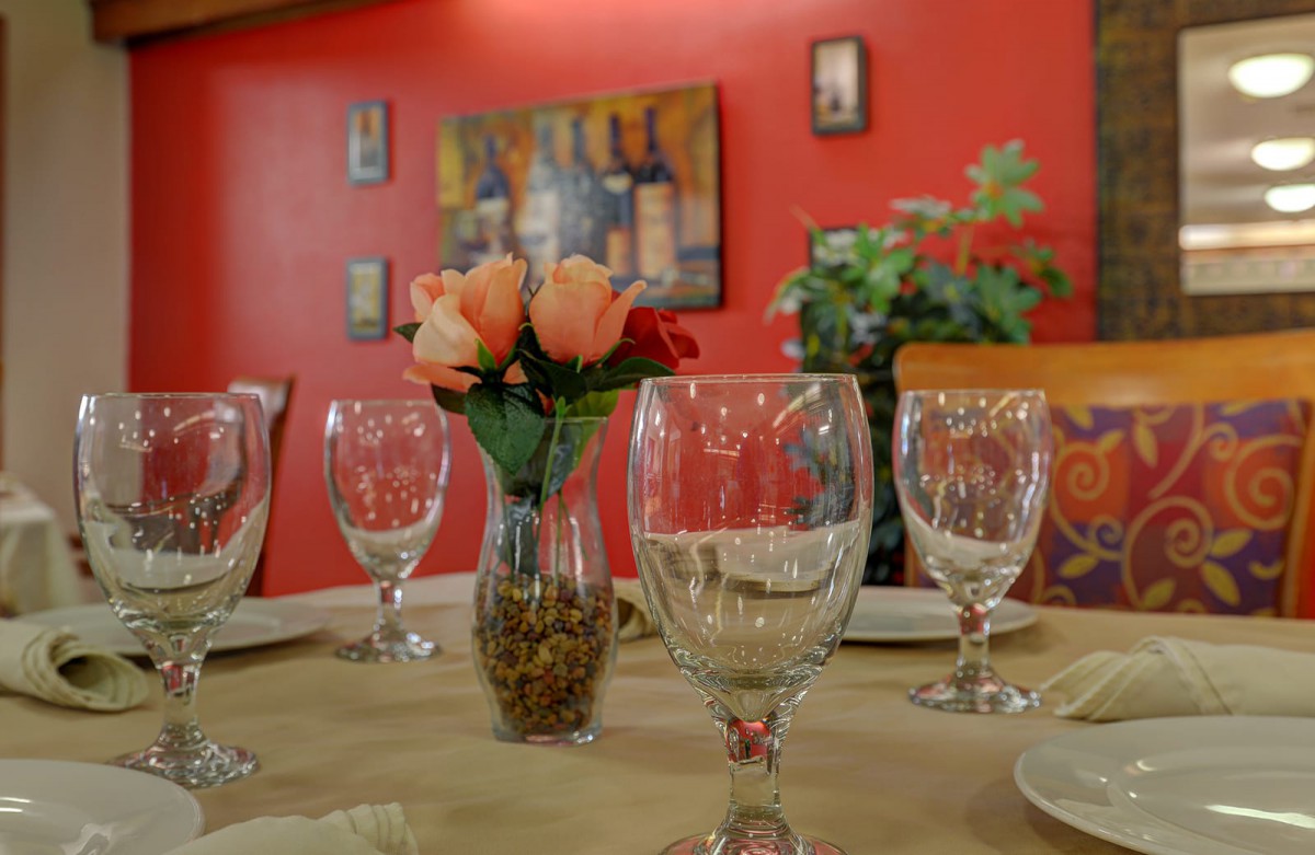 A cozy restaurant table setting with wine glasses and a floral centerpiece against a vibrant red wall.