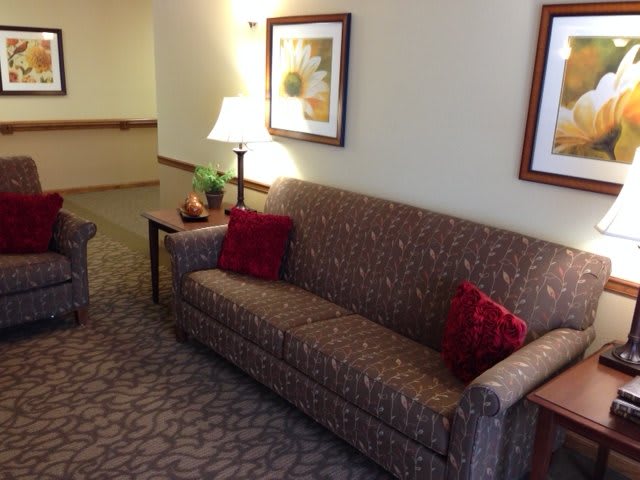 A cozy living room area featuring a patterned sofa with red cushions, a side table with a lamp, and framed artwork on the wall.
