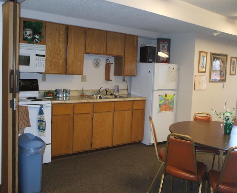 A small kitchen and dining area with wooden cabinets, a refrigerator, microwave, sink, and a round dining table with chairs.