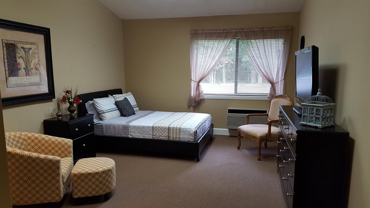 A neatly arranged bedroom with a bed, chair, and dresser by the window.