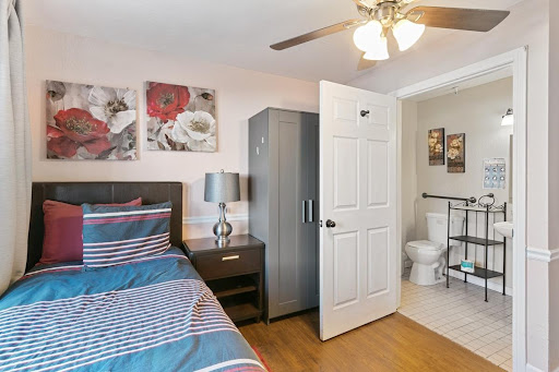 A cozy bedroom featuring a striped bedspread, modern furniture, and an adjacent bathroom.